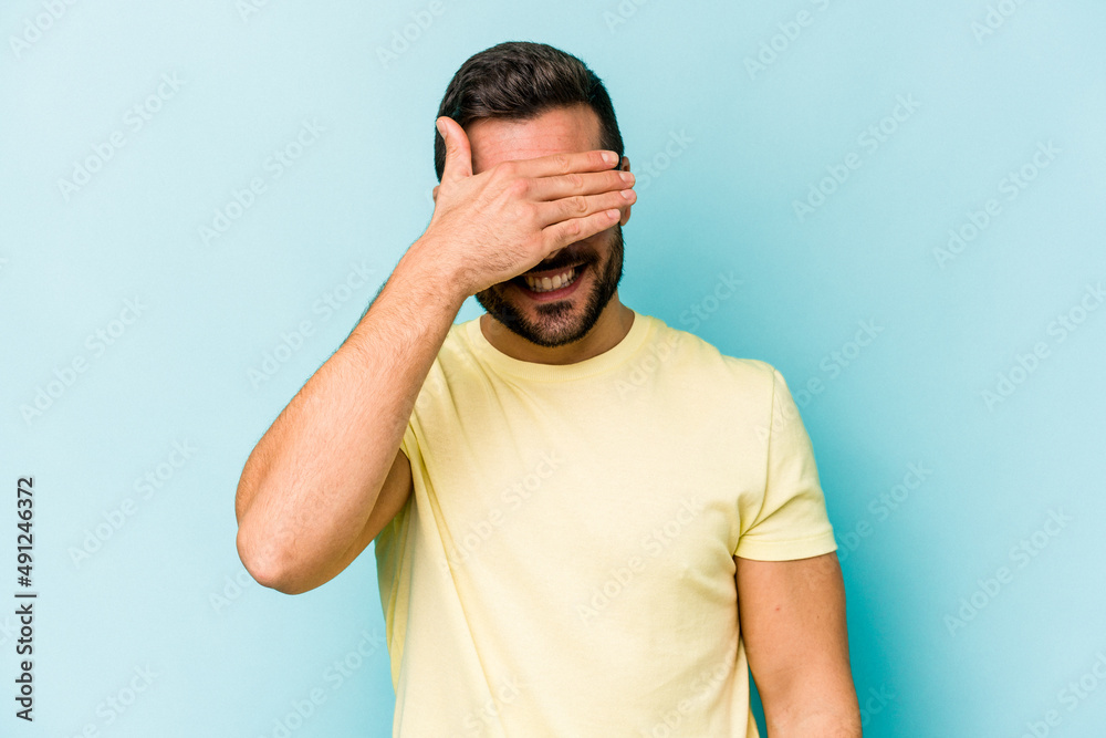 Young caucasian man isolated on blue background covers eyes with hands, smiles broadly waiting for a surprise. Young caucasian man isolated on blue background covers eyes with hands, smiles broadly waiting for a surprise.
