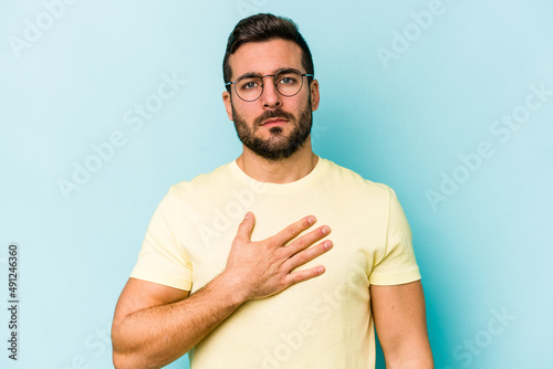 Young caucasian man isolated on blue background taking an oath, putting hand on chest.