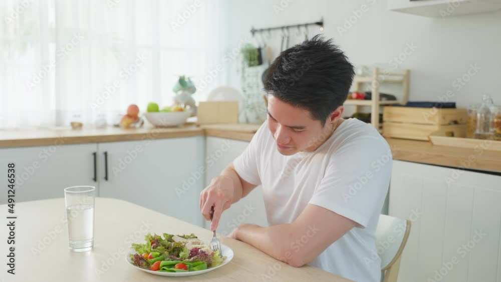 Asian attractive handsome male eating green salad in kitchen at home. Asian attractive handsome male eating green salad in kitchen at home.