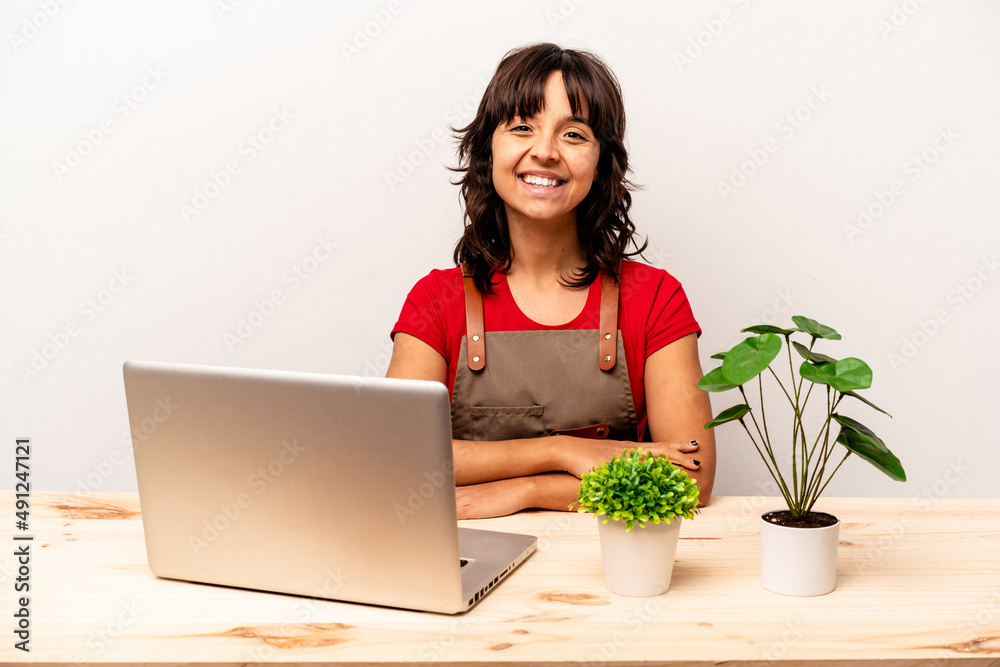 Young gardener hispanic woman sitting on a table isolated on white background happy, smiling and cheerful. Young gardener hispanic woman sitting on a table isolated on white background happy, smiling and cheerful.