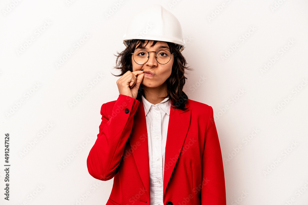 Young architect hispanic woman with helmet isolated on white background with fingers on lips keeping a secret. Young architect hispanic woman with helmet isolated on white background with fingers on lips keeping a secret.