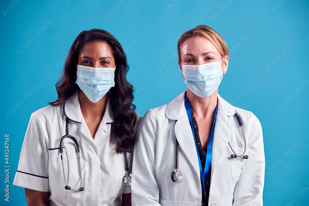 Portrait Of Female Doctor And Nurse Wearing Face Masks Standing In Front Of Blue Studio Background Portrait Of Female Doctor And Nurse Wearing Face Masks Standing In Front Of Blue Studio Background