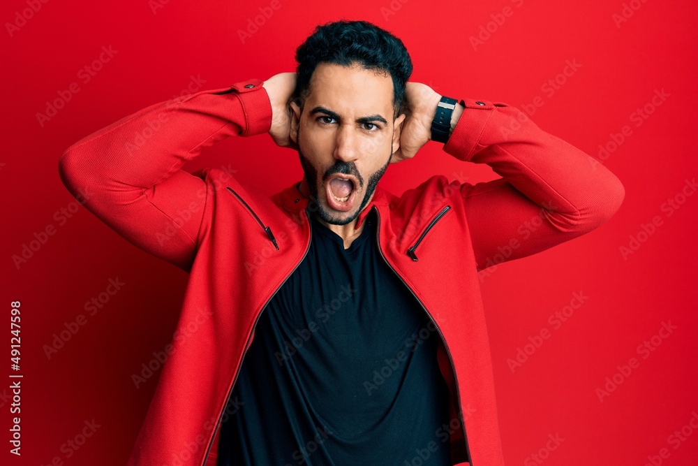 Young hispanic man wearing red leather jacket crazy and scared with hands on head, afraid and surprised of shock with open mouth Young hispanic man wearing red leather jacket crazy and scared with hands on head, afraid and surprised of shock with open mouth
