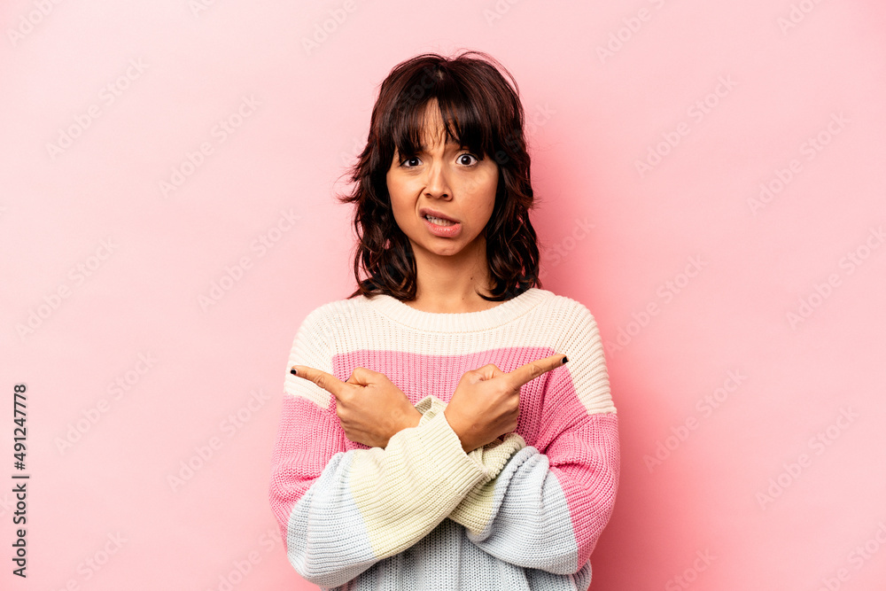 Young hispanic woman isolated on pink background points sideways, is trying to choose between two options. Young hispanic woman isolated on pink background points sideways, is trying to choose between two options.