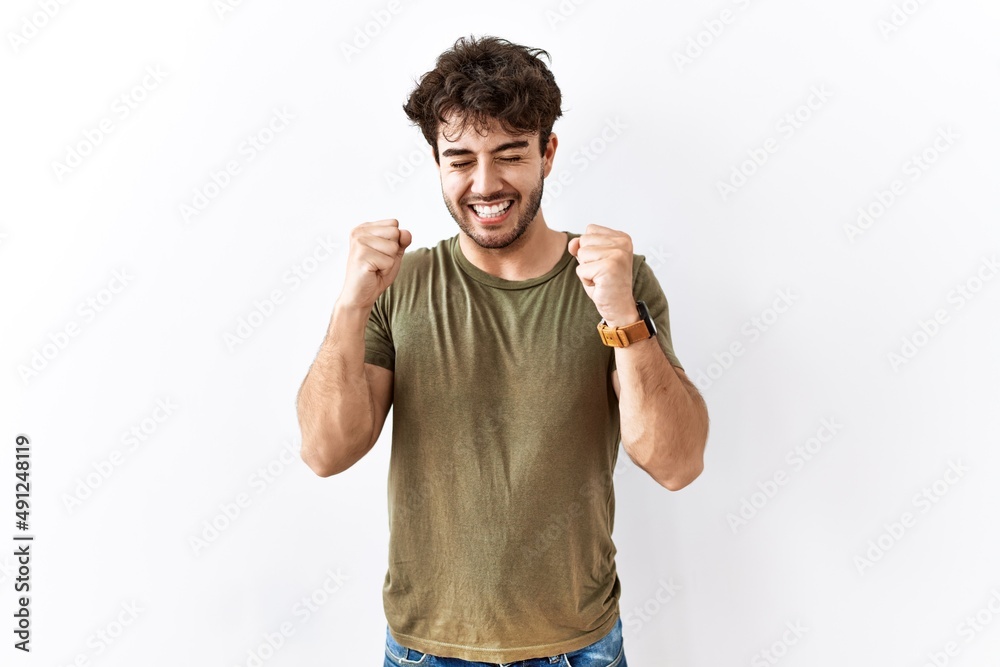 Fototapeta premium Hispanic man standing over isolated white background excited for success with arms raised and eyes closed celebrating victory smiling. winner concept.