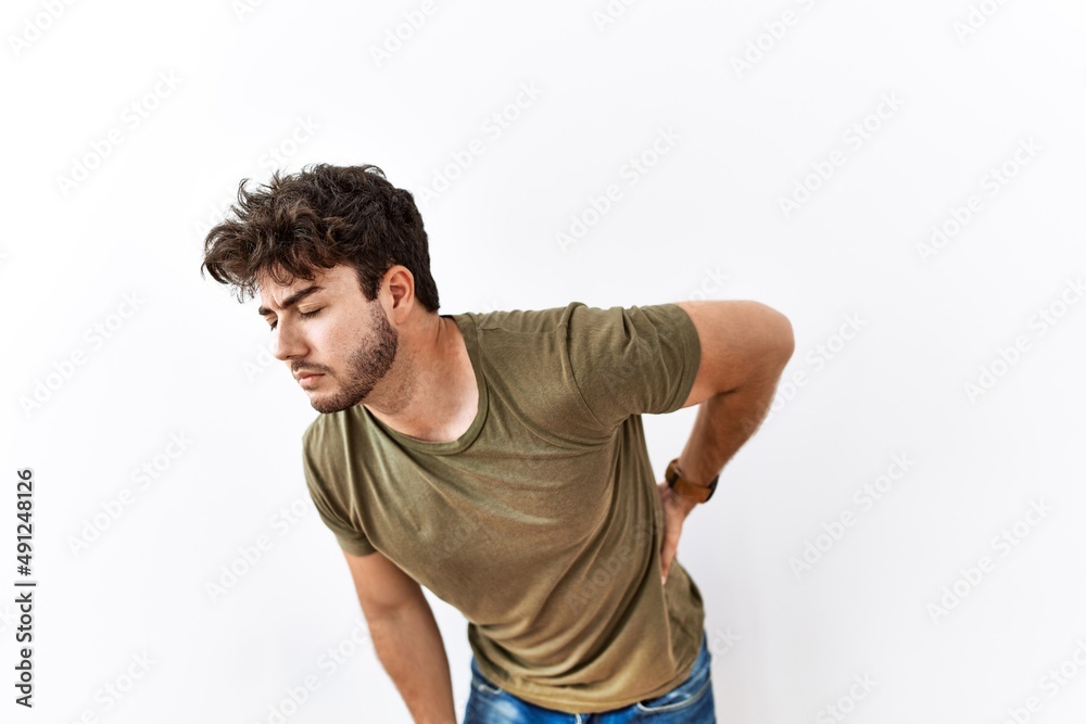 Hispanic man standing over isolated white background suffering of backache, touching back with hand, muscular pain Hispanic man standing over isolated white background suffering of backache, touching back with hand, muscular pain