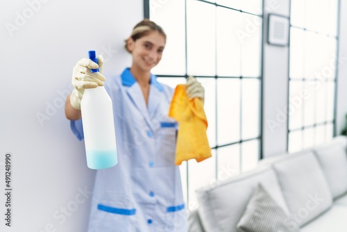 Young caucasian woman wearing cleaner uniform holding clean products at home