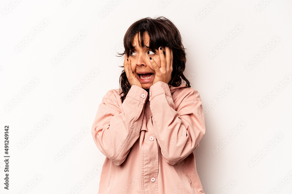Young hispanic woman isolated on white background covering ears with hands trying not to hear too loud sound.