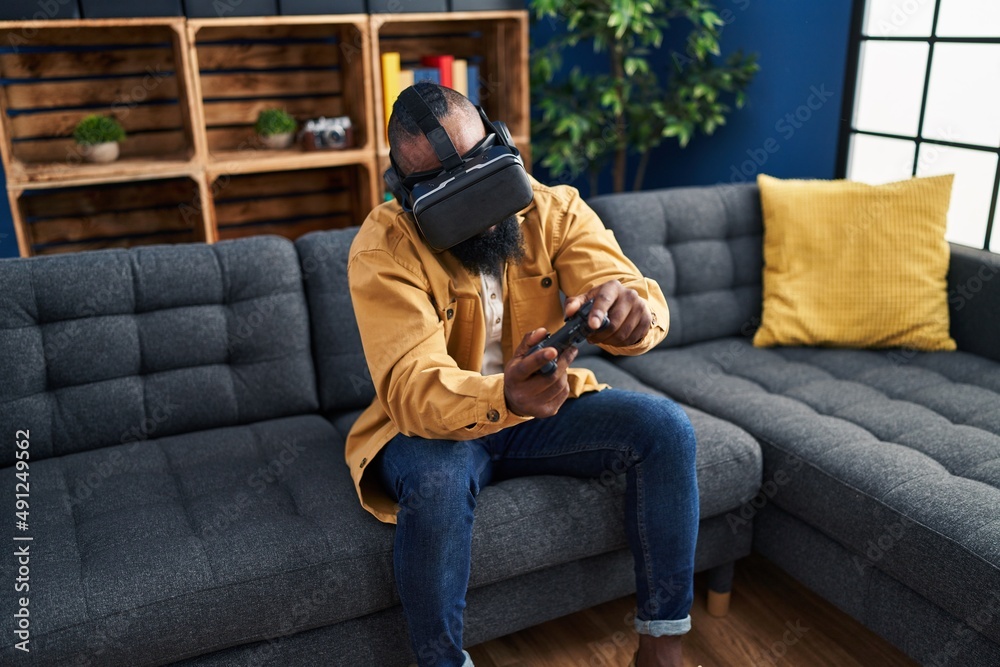 Obraz premium Young african american man playing video game using virtual reality glasses at home