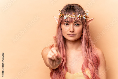 Young elf woman with pink hair isolated on beige background showing number one with finger.