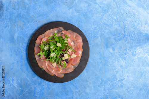 Beef or smoked turkey carpaccio with mixed salad and parmesan. On a blue background, top view, space for text