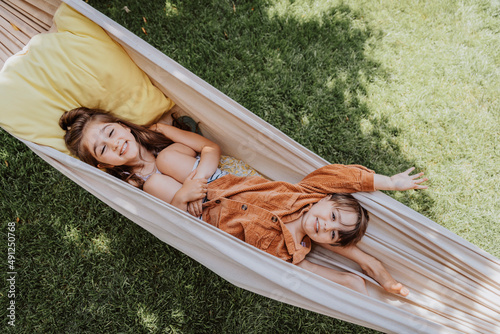 Smiling sister and brother lying in hammock at back yard photo