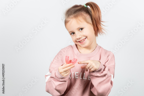Cute little girl with blond hair is holding a pink dental myofunctional trainer photo