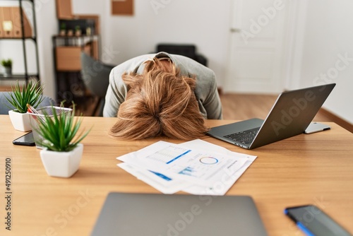 Middle age businesswoman overworked with head on desk at the office.
