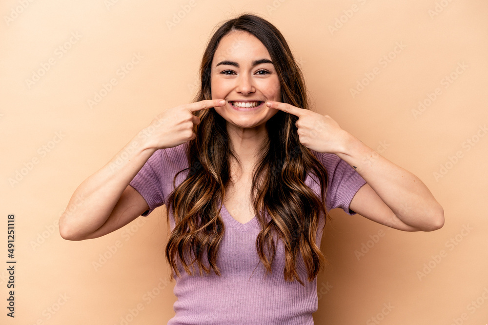 Young caucasian woman isolated on beige background smiles, pointing fingers at mouth. Young caucasian woman isolated on beige background smiles, pointing fingers at mouth.