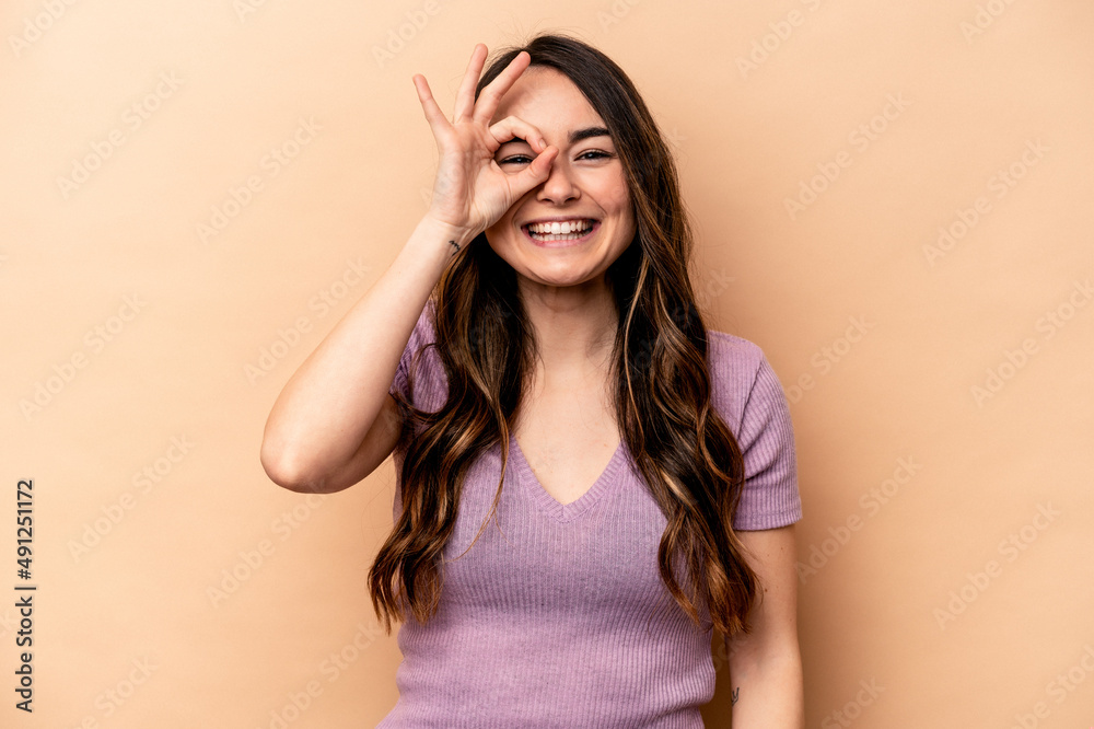 Young caucasian woman isolated on beige background excited keeping ok gesture on eye. Young caucasian woman isolated on beige background excited keeping ok gesture on eye.