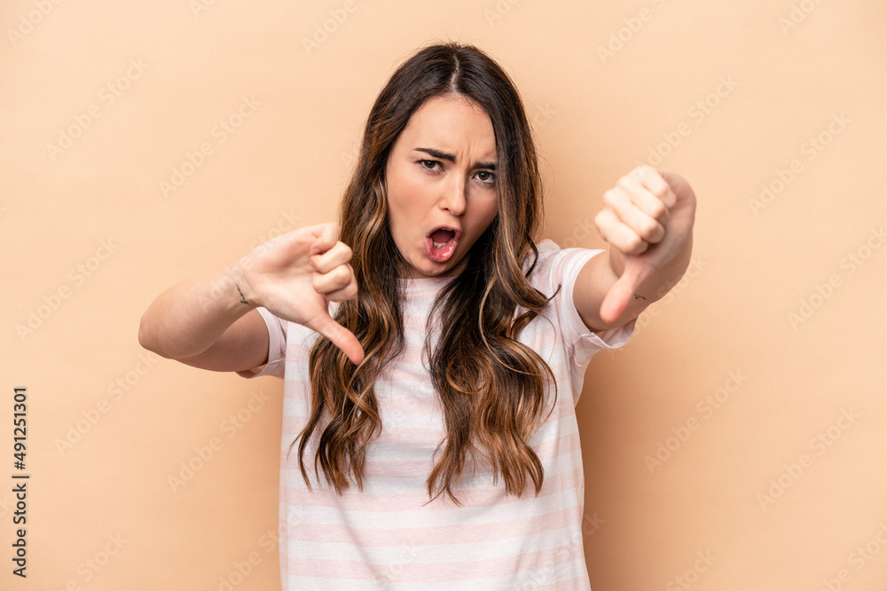 Fototapeta premium Young caucasian woman isolated on beige background showing thumb down and expressing dislike.