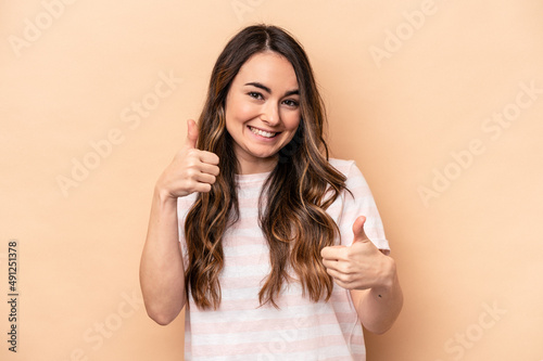 Young caucasian woman isolated on beige background raising both thumbs up, smiling and confident.