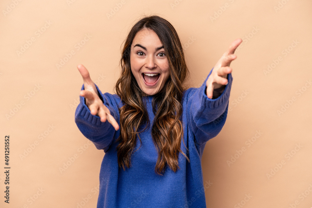 Young caucasian woman isolated on beige background feels confident giving a hug to the camera.
