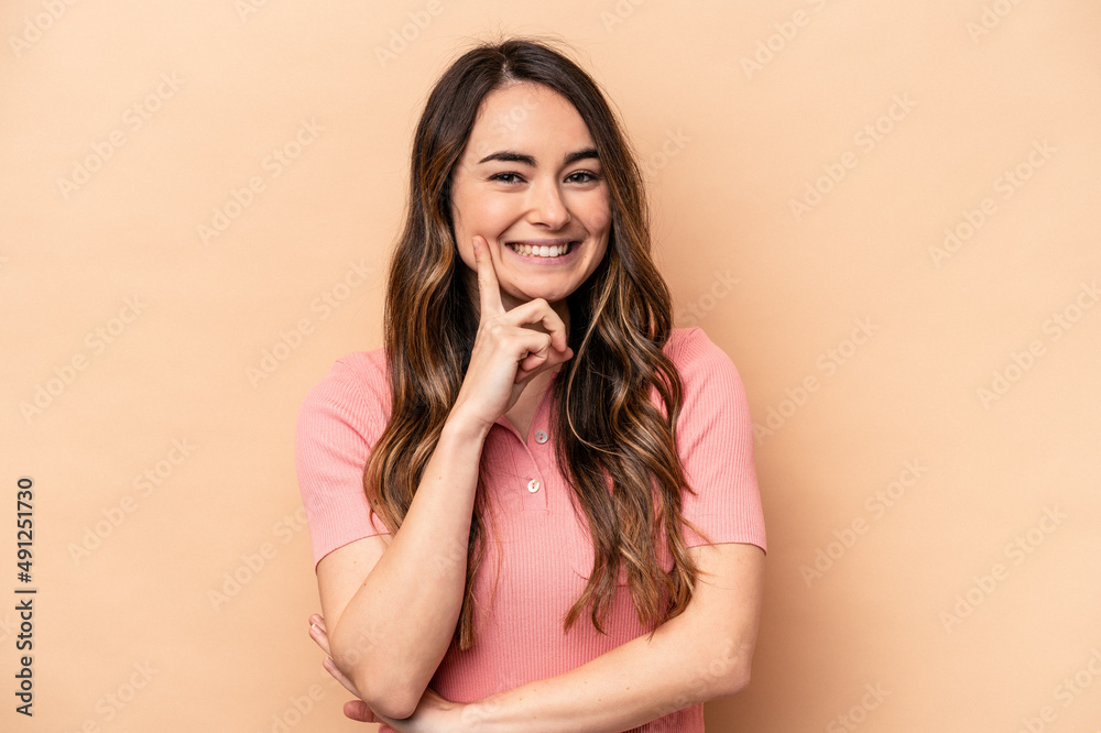 Fototapeta premium Young caucasian woman isolated on beige background smiling happy and confident, touching chin with hand.