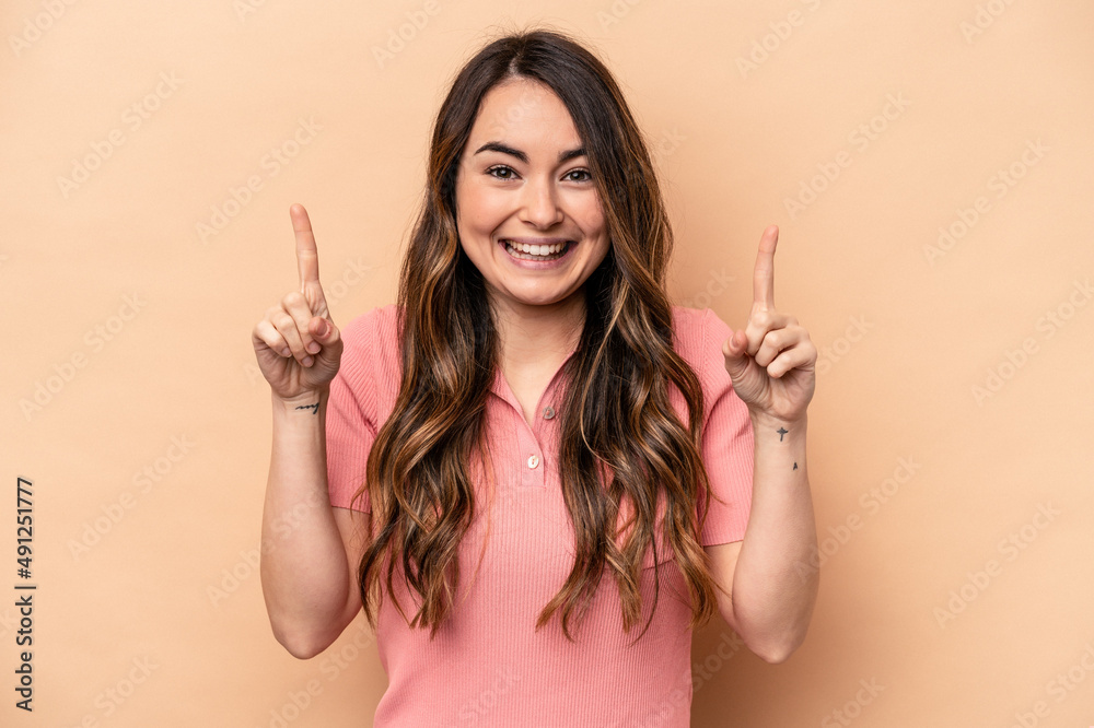 Young caucasian woman isolated on beige background indicates with both fore fingers up showing a blank space. Young caucasian woman isolated on beige background indicates with both fore fingers up showing a blank space.