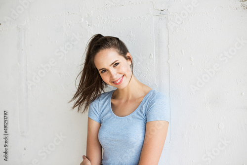 Happy woman with ponytail standing in front of wall photo