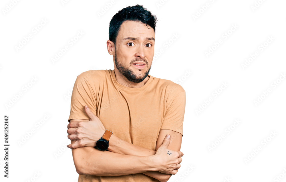 Fototapeta premium Hispanic man with beard wearing casual t shirt shaking and freezing for winter cold with sad and shock expression on face