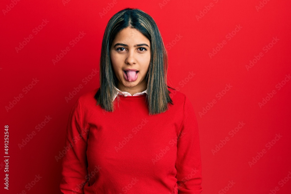 Young latin woman wearing casual clothes sticking tongue out happy with funny expression. emotion concept. Young latin woman wearing casual clothes sticking tongue out happy with funny expression. emotion concept.