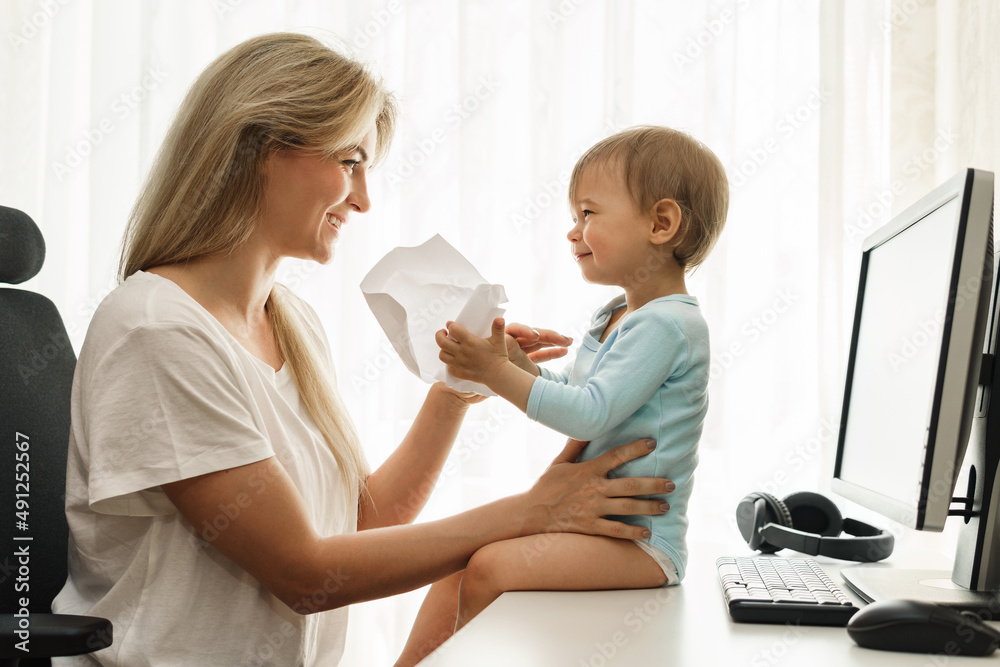 Little boy sitting on a desk distracting freelancer mother from paperwork. Little boy sitting on a desk distracting freelancer mother from paperwork.