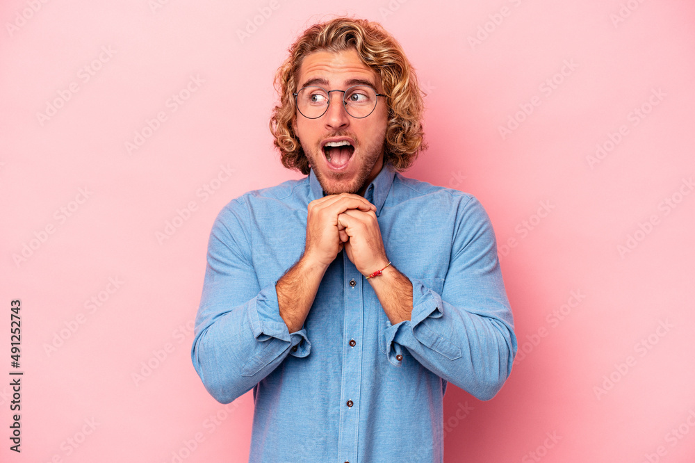 Young caucasian man isolated on pink background keeps hands under chin, is looking happily aside. Young caucasian man isolated on pink background keeps hands under chin, is looking happily aside.