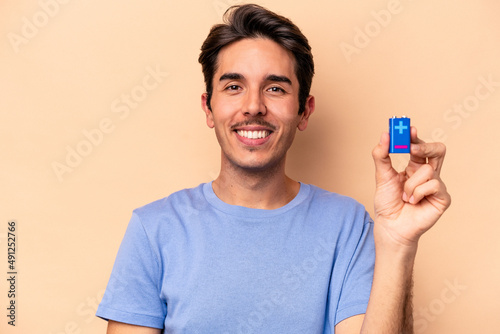 Young caucasian man holding a batterie isolated on beige background happy, smiling and cheerful. © Asier