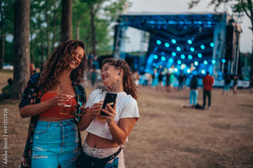 Two beautiful friends using a smartphone on a music festival