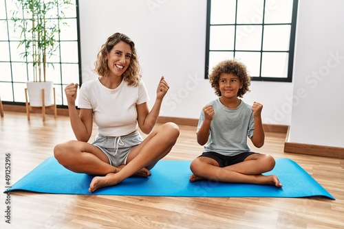 Young woman and son sitting on training mat at the gym screaming proud, celebrating victory and success very excited with raised arms