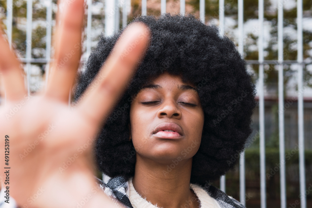 Afro woman with eyes closed showing palm in front of fence Afro woman with eyes closed showing palm in front of fence