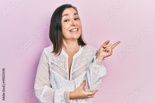 Middle age hispanic woman wearing casual clothes with a big smile on face, pointing with hand and finger to the side looking at the camera.