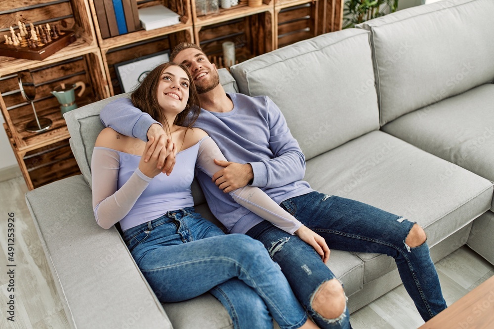 Fototapeta premium Young caucasian couple relaxed sitting on the sofa hugging at home.