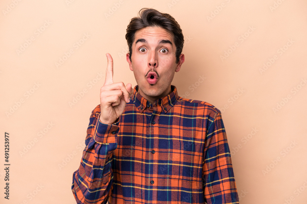 Young caucasian man isolated on beige background pointing upside with opened mouth.