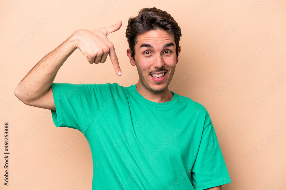 Obraz premium Young caucasian man isolated on beige background person pointing by hand to a shirt copy space, proud and confident