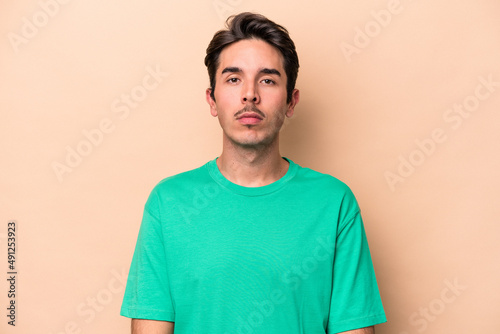Young caucasian man isolated on beige background sad, serious face, feeling miserable and displeased.