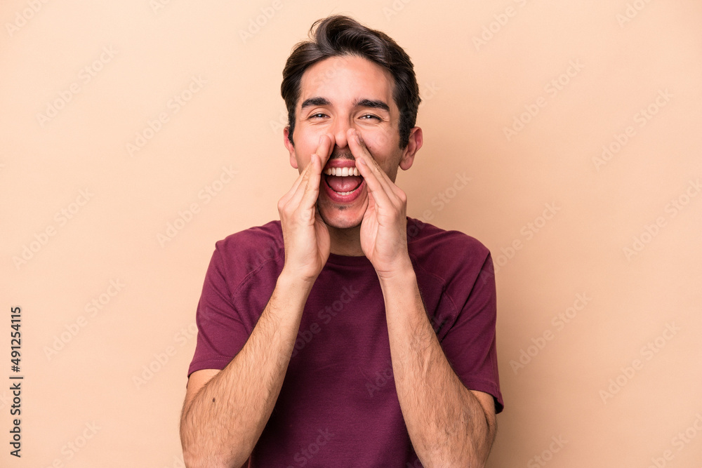 Young caucasian man isolated on beige background saying a gossip, pointing to side reporting something. Young caucasian man isolated on beige background saying a gossip, pointing to side reporting something.