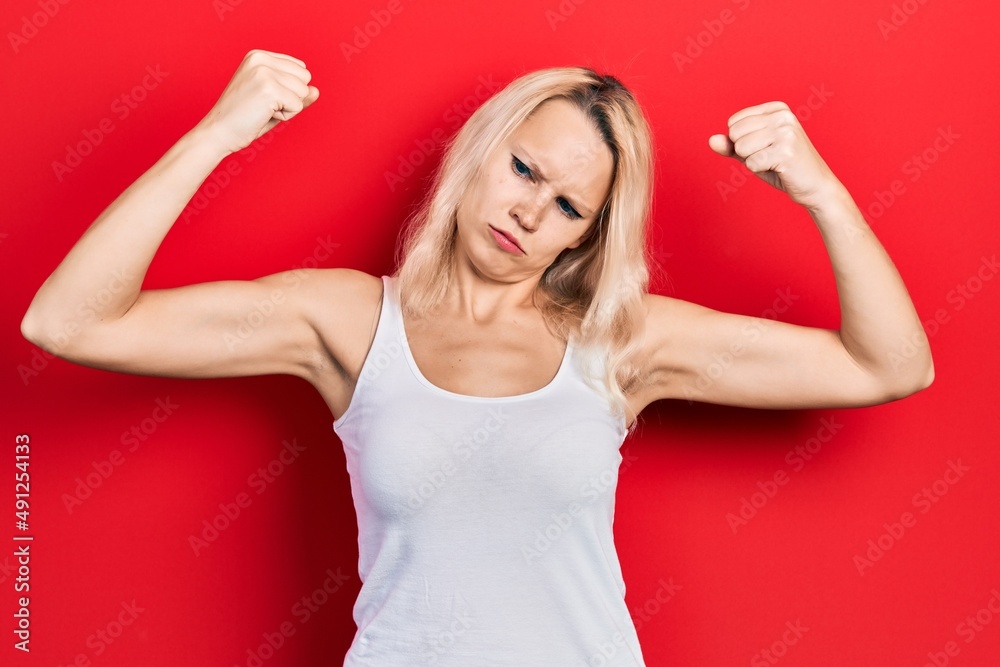 Beautiful caucasian blonde woman wearing casual white t shirt showing arms muscles smiling proud. fitness concept. Beautiful caucasian blonde woman wearing casual white t shirt showing arms muscles smiling proud. fitness concept.