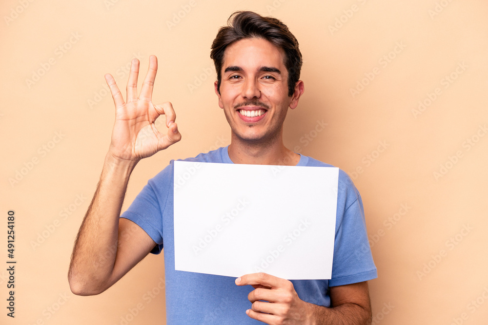 Young caucasian man holding a placard isolated on beige background cheerful and confident showing ok gesture. Young caucasian man holding a placard isolated on beige background cheerful and confident showing ok gesture.