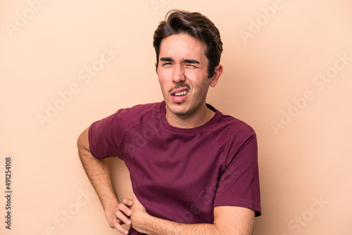 Young caucasian man isolated on beige background having a liver pain, stomach ache.