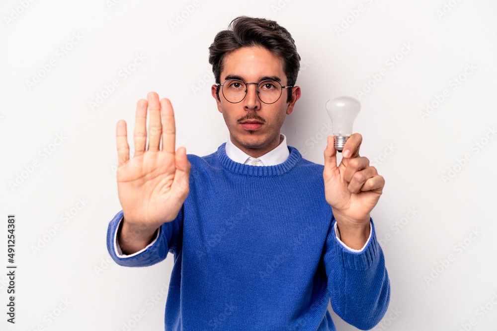 Young caucasian man holding a lightbulb isolated on white background standing with outstretched hand showing stop sign, preventing you. Young caucasian man holding a lightbulb isolated on white background standing with outstretched hand showing stop sign, preventing you.
