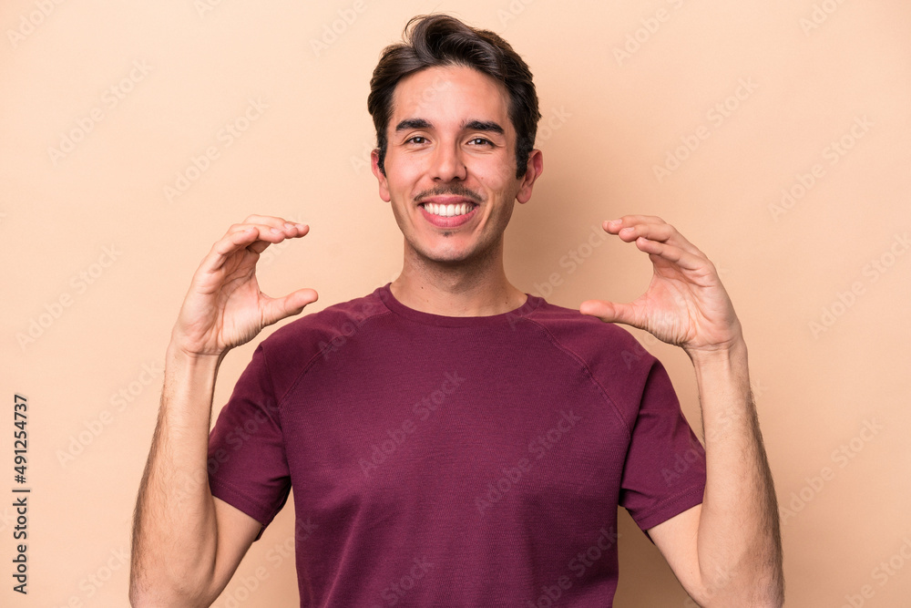 Young caucasian man isolated on beige background holding something with palms, offering to camera. Young caucasian man isolated on beige background holding something with palms, offering to camera.
