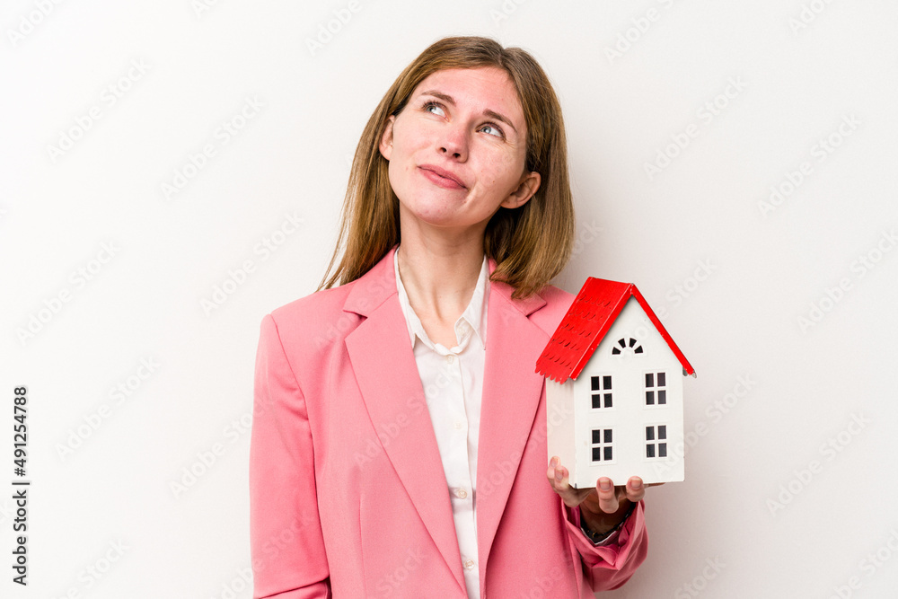 Young business English woman holding house toy isolated on white background dreaming of achieving goals and purposes Young business English woman holding house toy isolated on white background dreaming of achieving goals and purposes