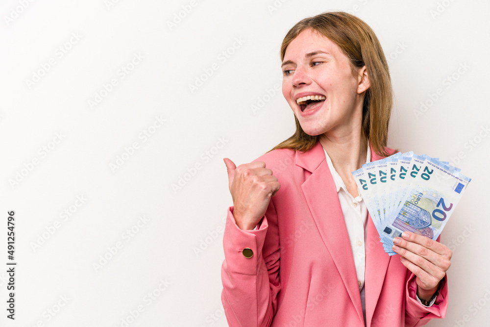 Young business English woman holding banknotes isolated on white background points with thumb finger away, laughing and carefree. Young business English woman holding banknotes isolated on white background points with thumb finger away, laughing and carefree.