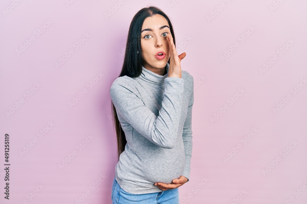 Beautiful woman with blue eyes expecting a baby, touching pregnant belly hand on mouth telling secret rumor, whispering malicious talk conversation Beautiful woman with blue eyes expecting a baby, touching pregnant belly hand on mouth telling secret rumor, whispering malicious talk conversation