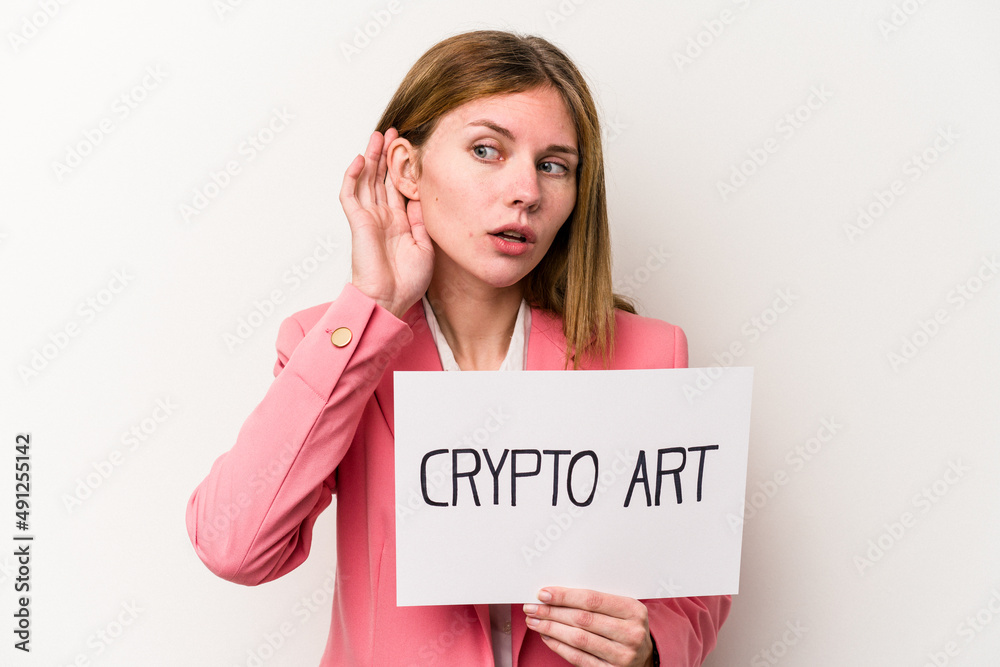 Young English business woman holding a crypto money placard isolated on white background trying to listening a gossip. Young English business woman holding a crypto money placard isolated on white background trying to listening a gossip.