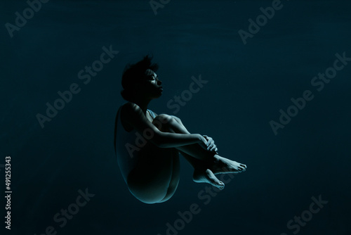 Young woman in fetal position swimming underwater photo